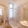 Bright bathroom with bathtub, shower curtain, washbasin and window.