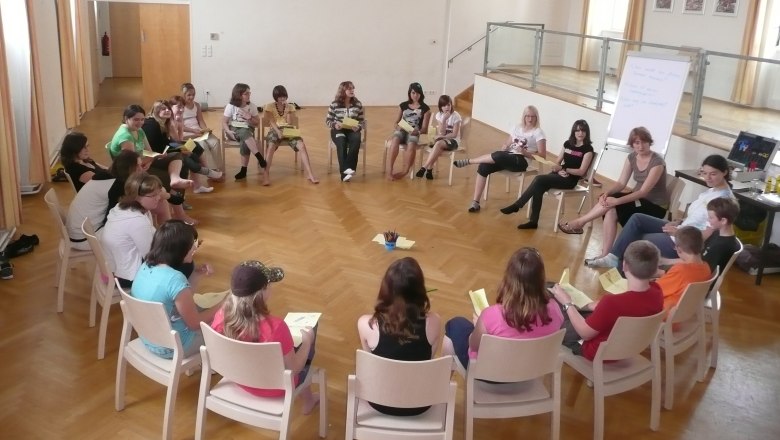 People sit in a circle of chairs in a large room.