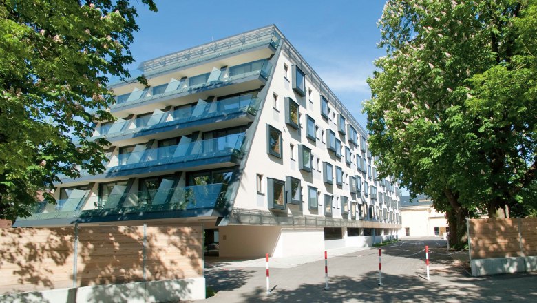 Modern hotel building with glass balconies and trees in the foreground.