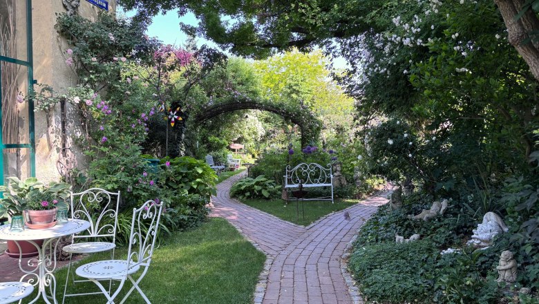 An idyllic garden with white garden furniture, a paved path and lush vegetation.