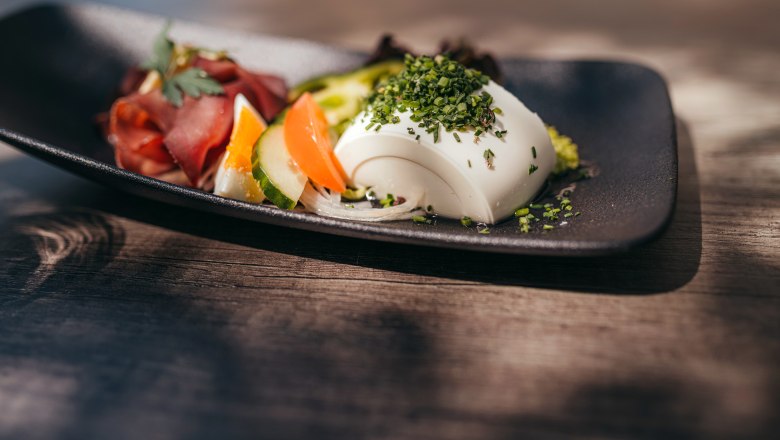 A plate of raw venison ham and vegetables, garnished with herbs.