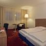 Double room with red carpeted floor, desk and large double bed.