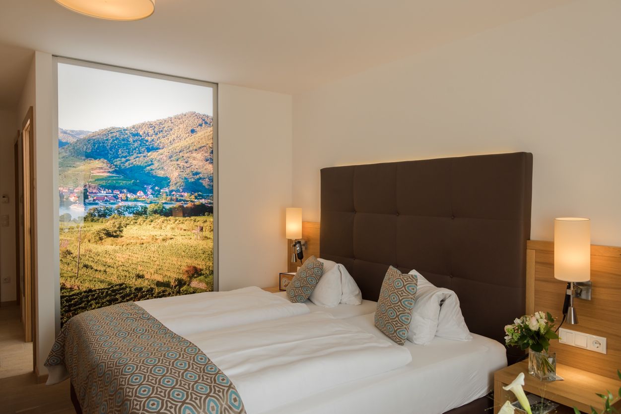 Modern hotel room with double bed, decorative cushions and large landscape picture on the wall.