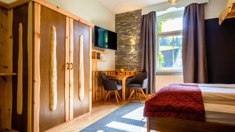 Cozy room with wooden furniture, stone wall, table and chairs, TV and window with curtains.