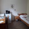 A simply furnished room with a bed, table, chair, fridge and coffee machine.