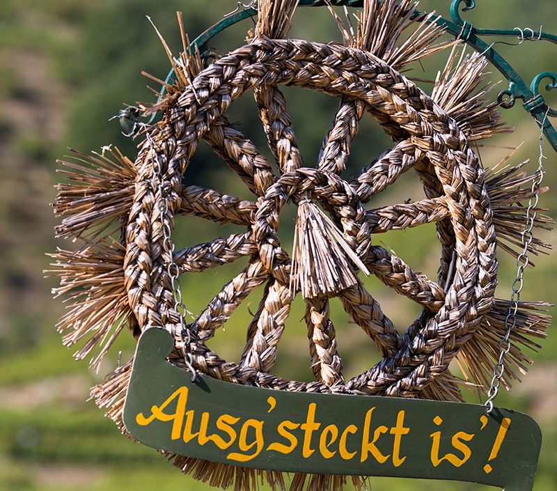A woven straw wreath with a sign saying 'Ausg'steckt is' hangs from a chain.