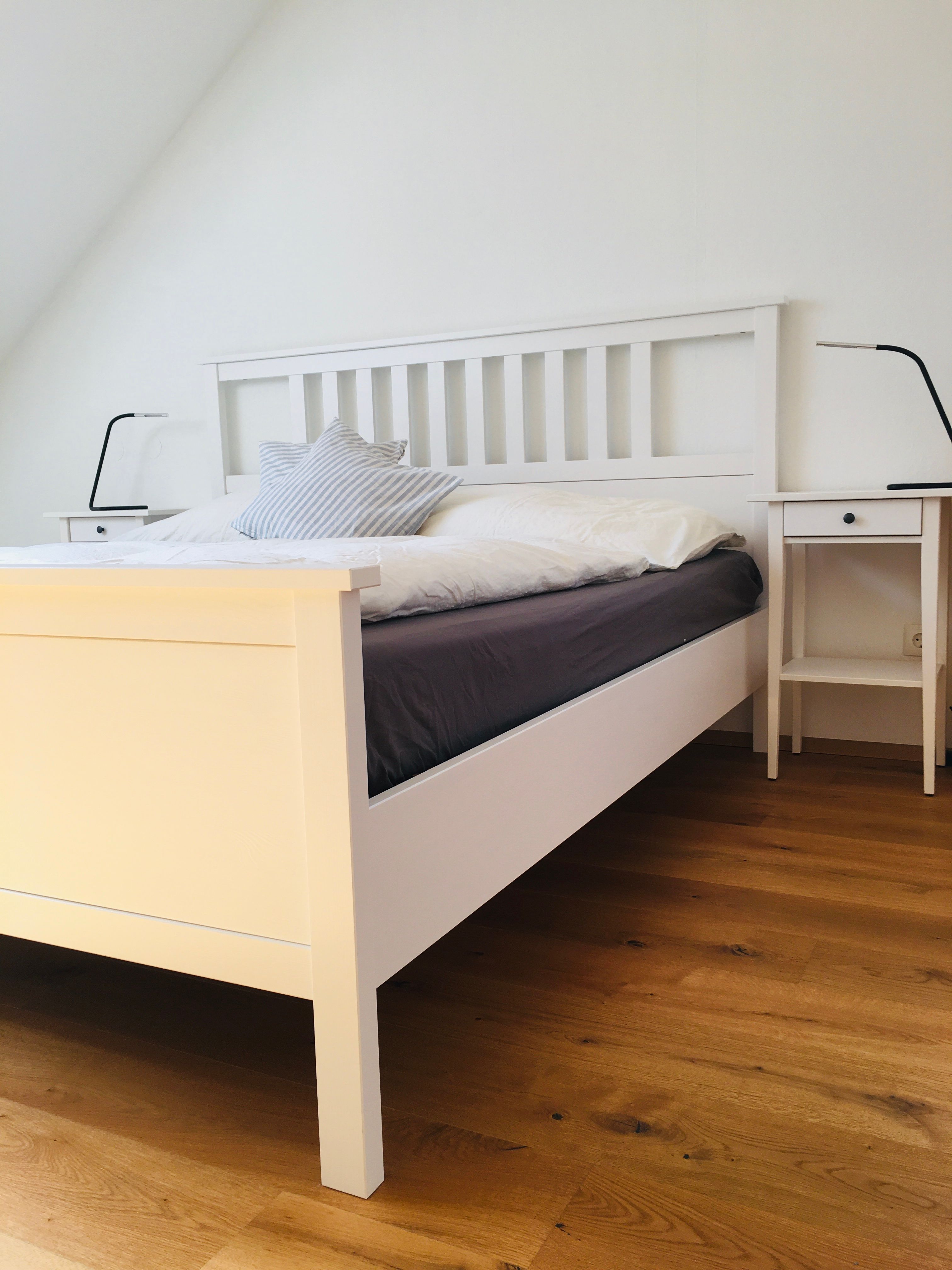 A simple bedroom with a white bed, two bedside tables and wooden flooring.