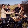 Four people clink glasses of wine while standing next to e-bikes in a vineyard.