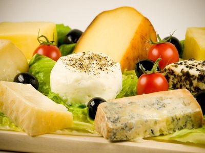 Various cheeses on a wooden board with tomatoes and olives.