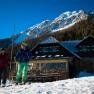 Two skiers in front of the Edelweissh&uuml;tte on the Schneeberg with a snow-covered mountain in the background.