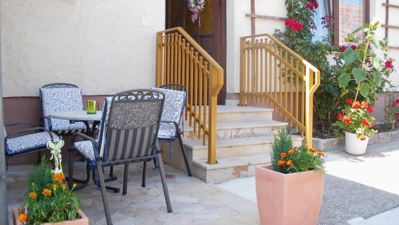 Entrance area of a vacation apartment with terrace, table and chairs, flowers and railings.