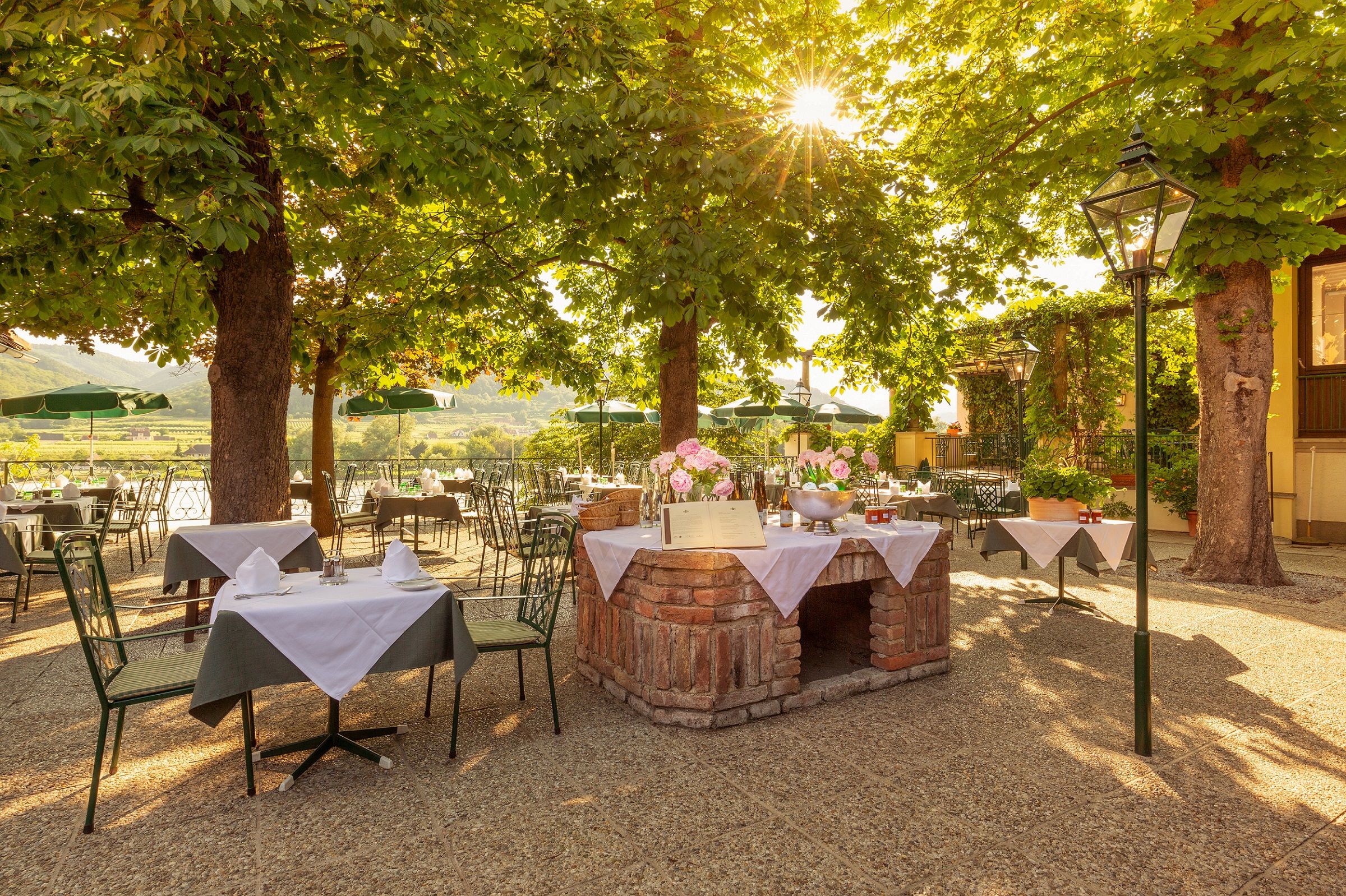 A sunny outdoor area of a restaurant with covered tables under trees.