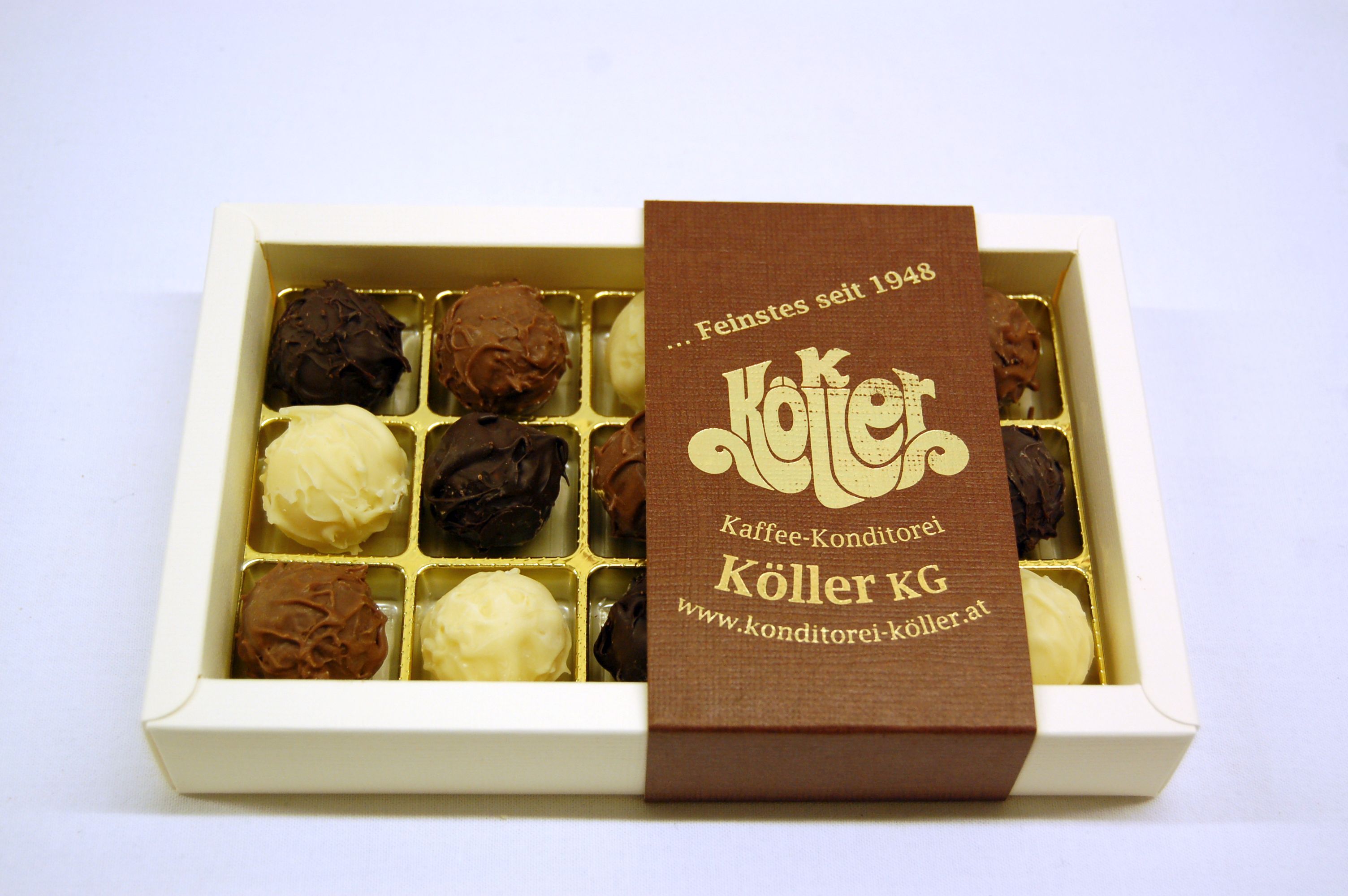 A box of handmade chocolates from Köller KG, partially opened, on a white background.