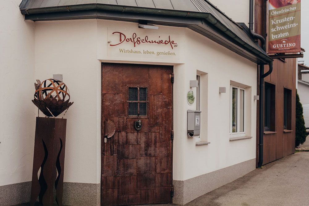 Entrance to an inn called Dorfschmiede with rustic door and decoration.