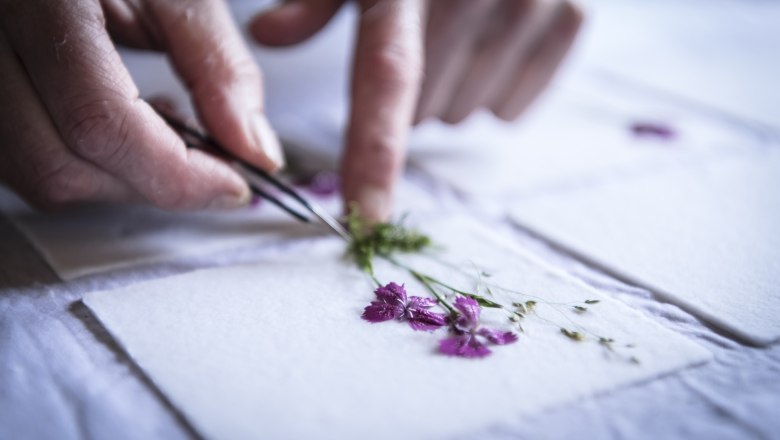 Close-up of hands placing flowers on paper with tweezers.