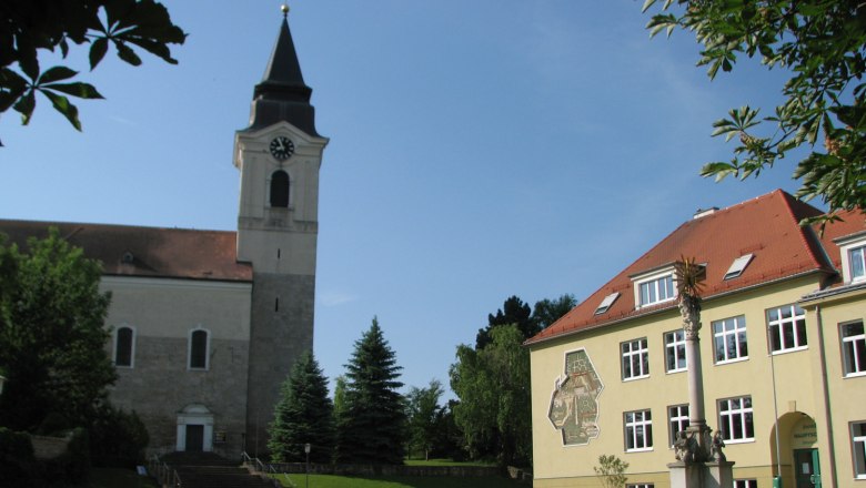 Church and building in Stronsdorf with clock tower and sunshine.