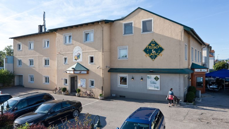 Pension Schlafgut, © Werner Jäger Exterior view of a building labeled 'Pension Schlafgut' and 'Café Trisch & Tratsch'. Cars are parked in front of it, a person with a baby carriage walks past.