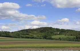 Landscape with hills and fields under a blue sky with clouds.