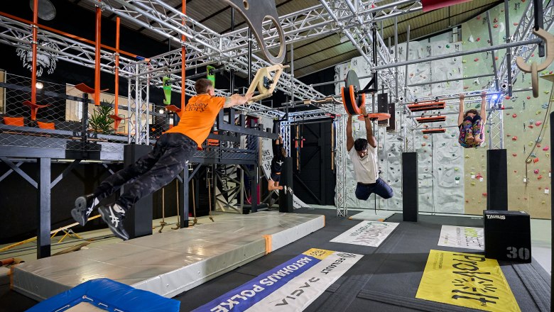 People train in an indoor climbing park with various obstacles and climbing walls.