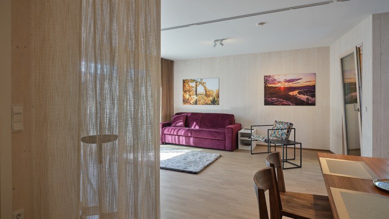 Living room with purple sofa, wooden table and chairs, curtain, and murals.