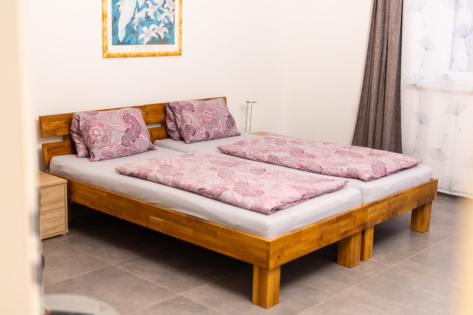 One bedroom with two single beds that stand together. The beds have pink patterned bed linen. A picture with a flower motif hangs on the wall.