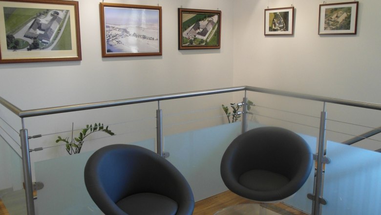 Modern interior with two black chairs and a glass table in front of a wall with framed pictures.