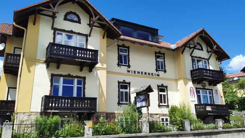 Yellow building with the inscription 'WIENERHEIM', wooden balconies and blue sky.