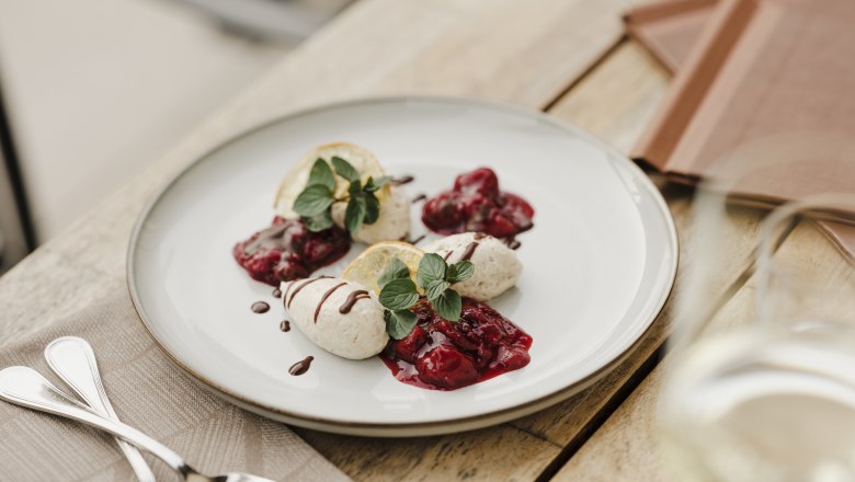 A plate of poppy seed mousse, garnished with berry compote and mint leaves, on a wooden table.