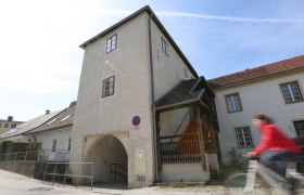 A historic building with an archway and a person on a bicycle in the foreground.