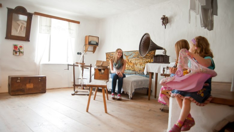 A room in the Langau Leisure Museum with antique furniture and a gramophone. Two children are sitting on a bench, a girl is sitting on a bed.