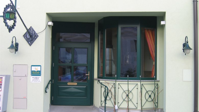 Entrance area of a building with green door and windows, decorated with plants and lanterns.