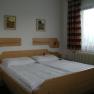 A simply furnished hotel room with a wooden double bed, two pictures on the wall and a window with curtains.