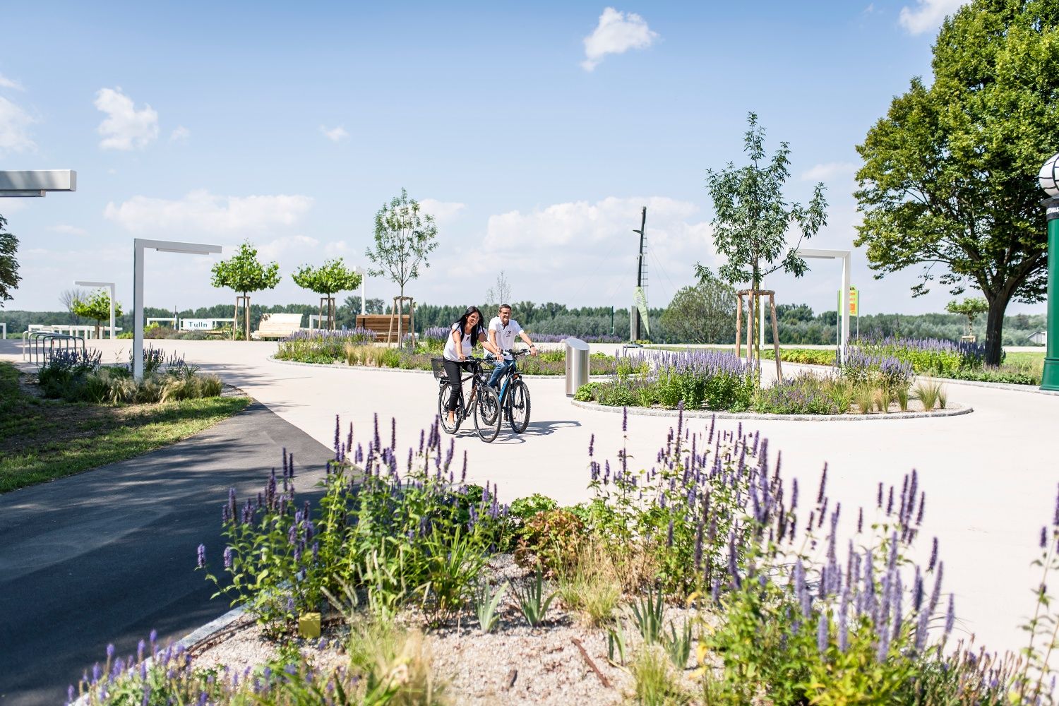 Two people ride bicycles through a park in bloom in Tulln an der Donau.