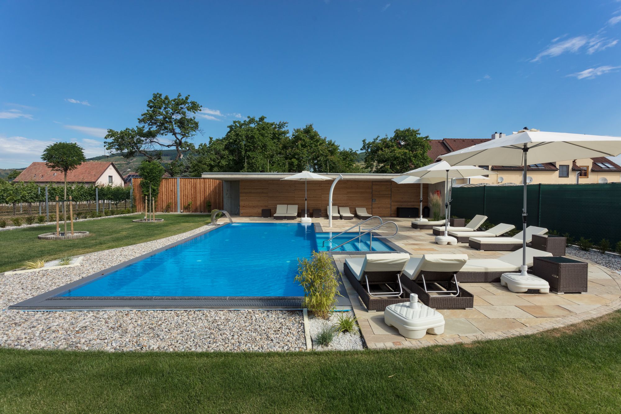 Modern outdoor pool with sun loungers and parasols in a well-tended garden.