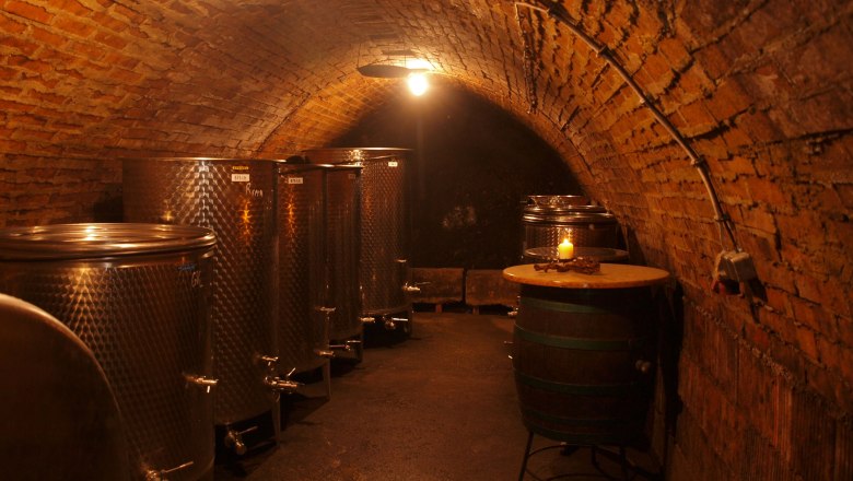 A wine cellar with metal tanks and a barrel, illuminated by warm light.