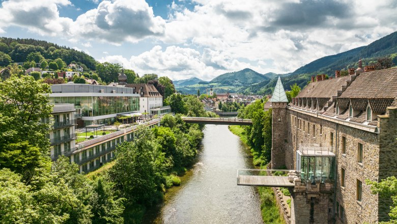 The castle on the Iron Road, © Dominik Stixenberger Panorama of a river landscape with a castle and modern architecture, surrounded by green hills.