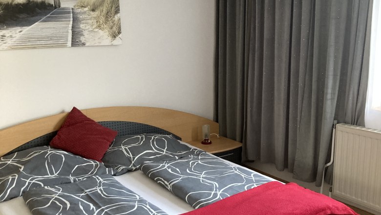 Bedroom with double bed, gray bed linen, red throw and pillows, lamp and beach picture on the wall.