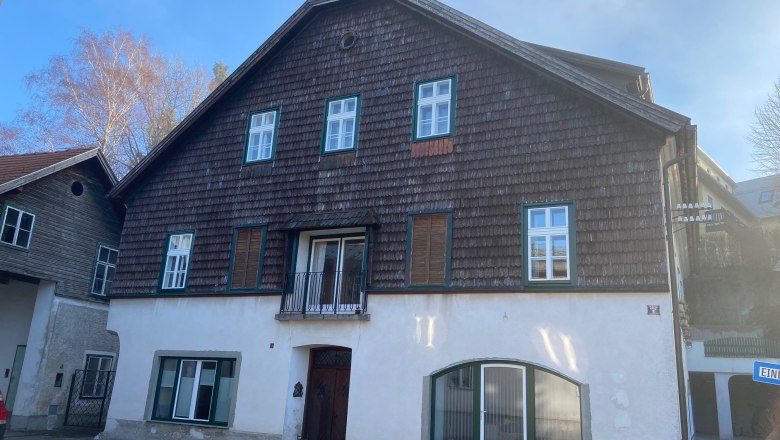 Traditional house with wooden shingles and white windows, blue sky in the background.
