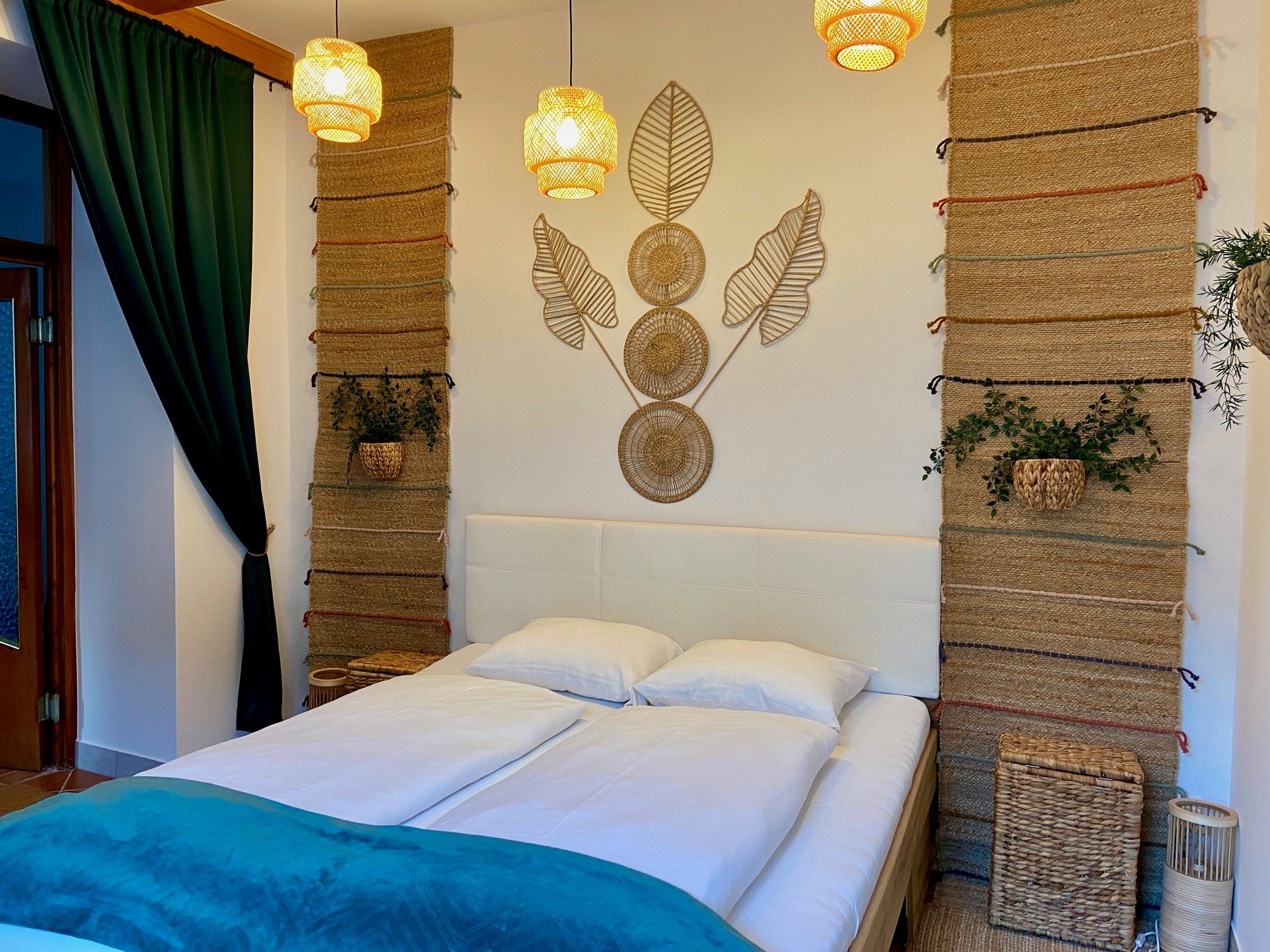 A cozy bedroom with a double bed, decorative tapestries and plants.