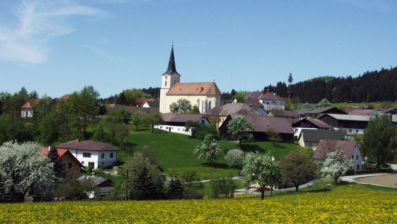 Landscape with church and village in the background, surrounded by blossoming trees and meadows.