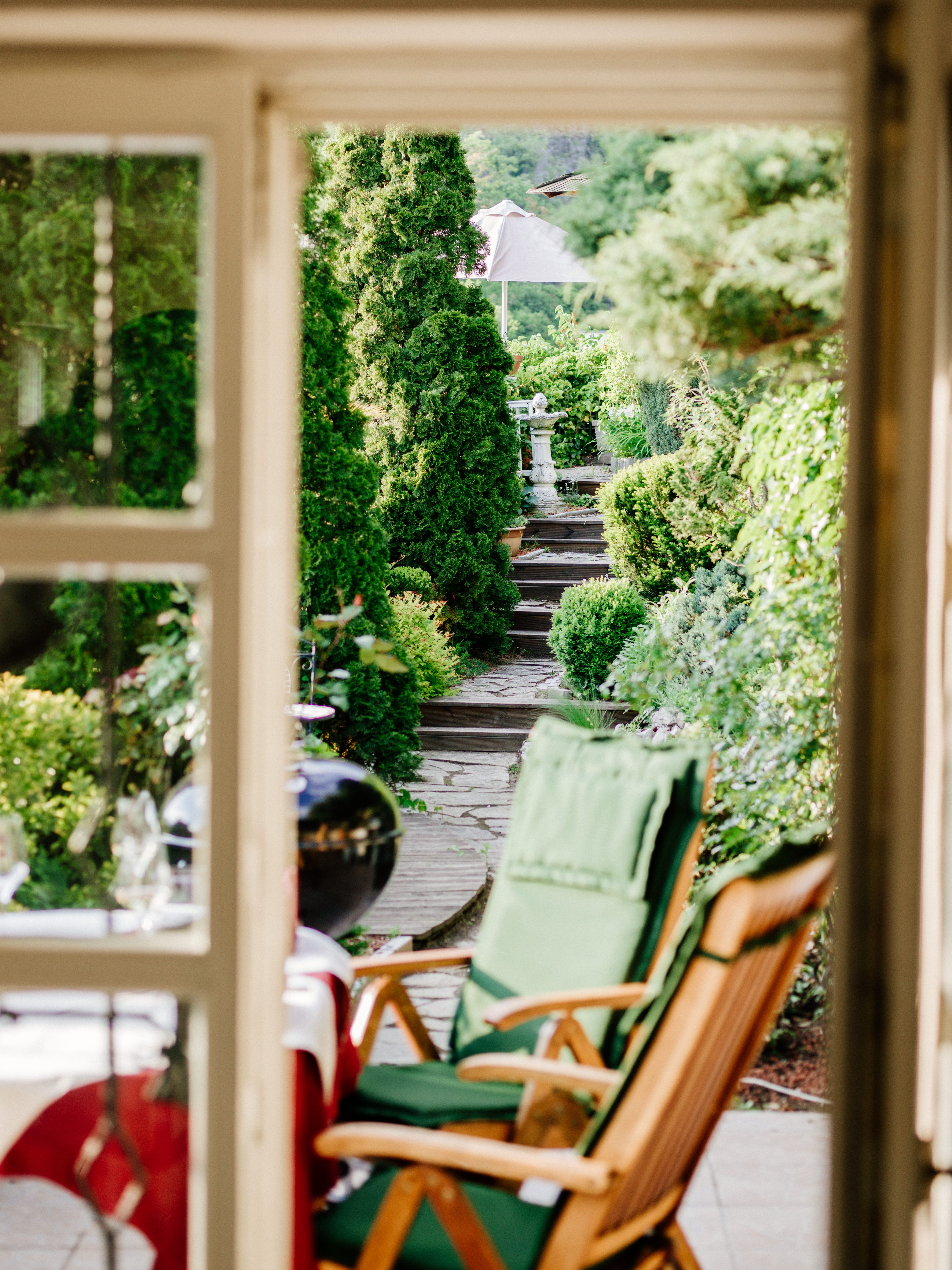 View through a door onto a green garden with chairs and a path.
