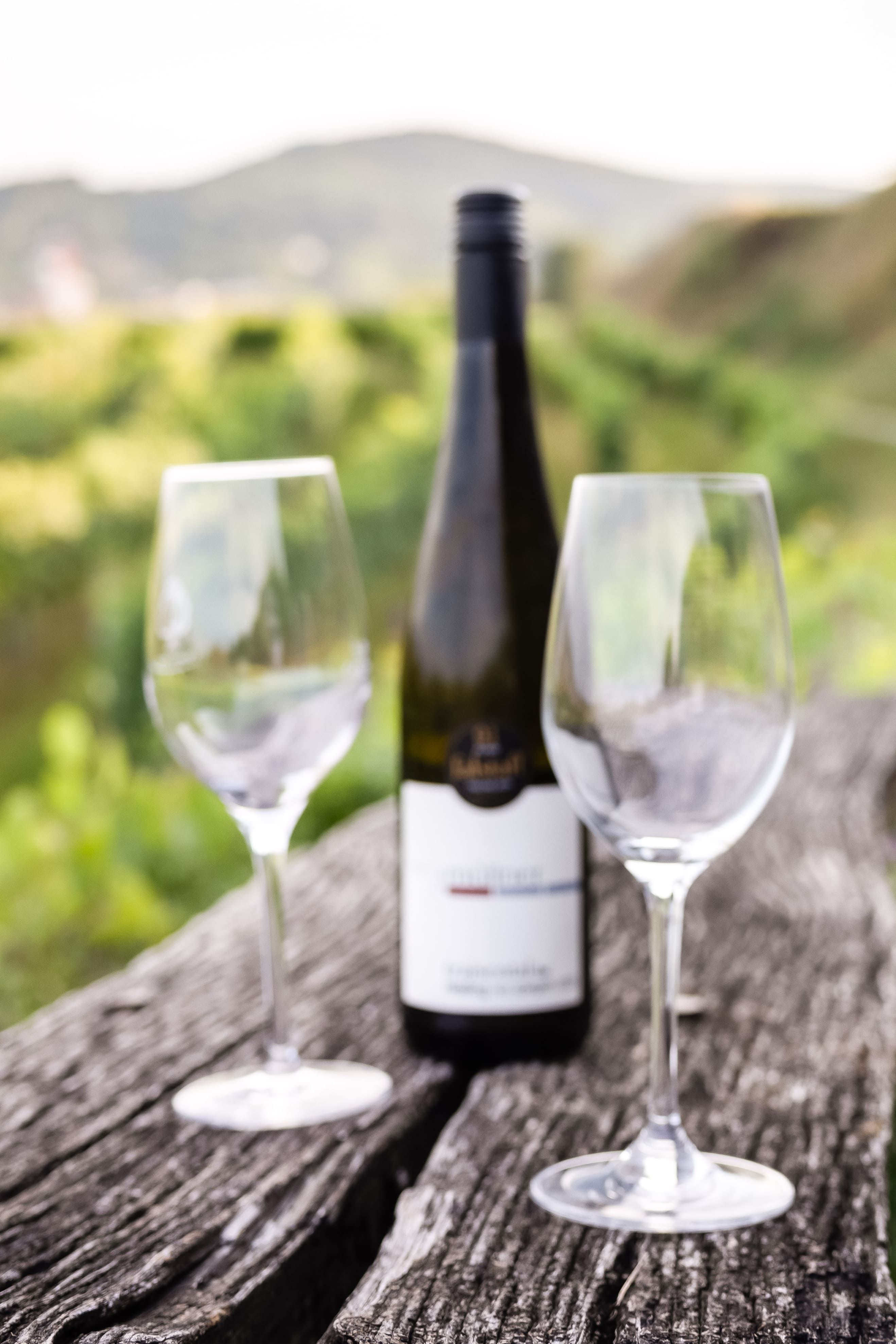 Two empty wine glasses and a wine bottle on a wooden table outdoors with a blurred background.