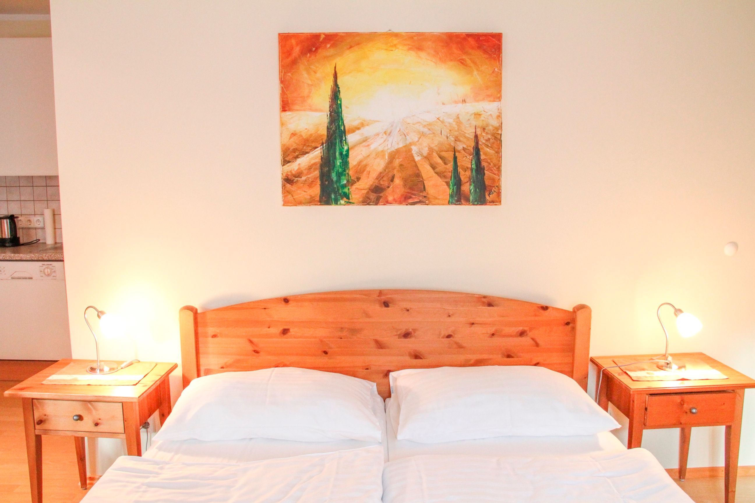 Bedroom with wooden bed, two bedside tables and a landscape painting on the wall.