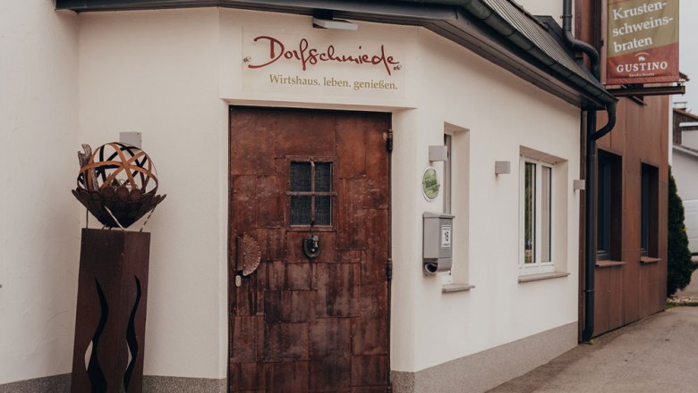 Entrance to an inn called Dorfschmiede with rustic door and decoration.