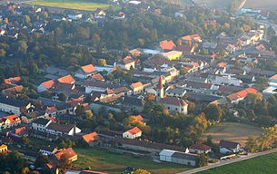 Aerial view of a village with church and houses, surrounded by trees and fields.