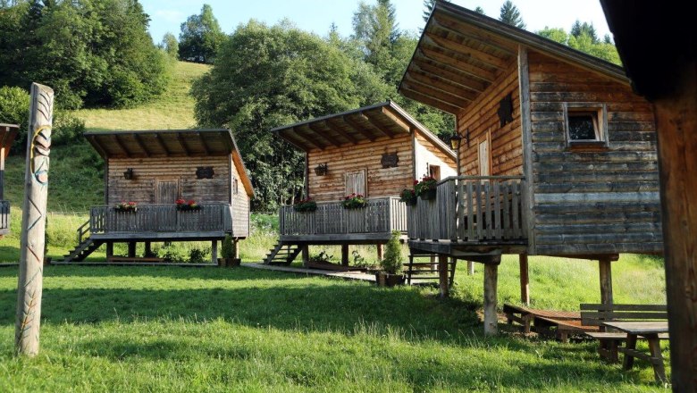Sulzbichl adventure village, © weinfranz.at Three wooden huts on stilts with verandas in a green, wooded area.