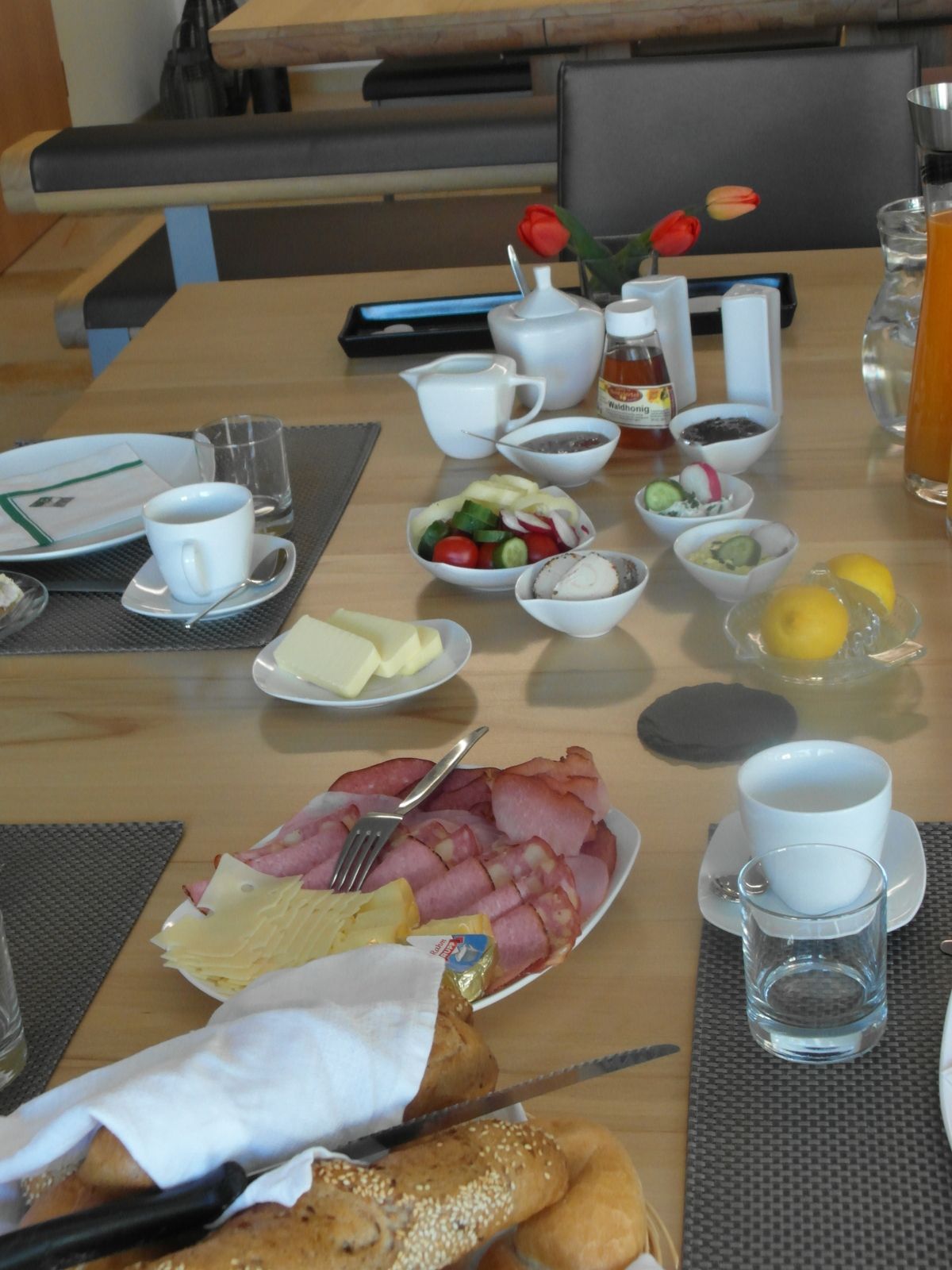 Breakfast table with cold cuts, cheese, bread rolls, vegetables and drinks.