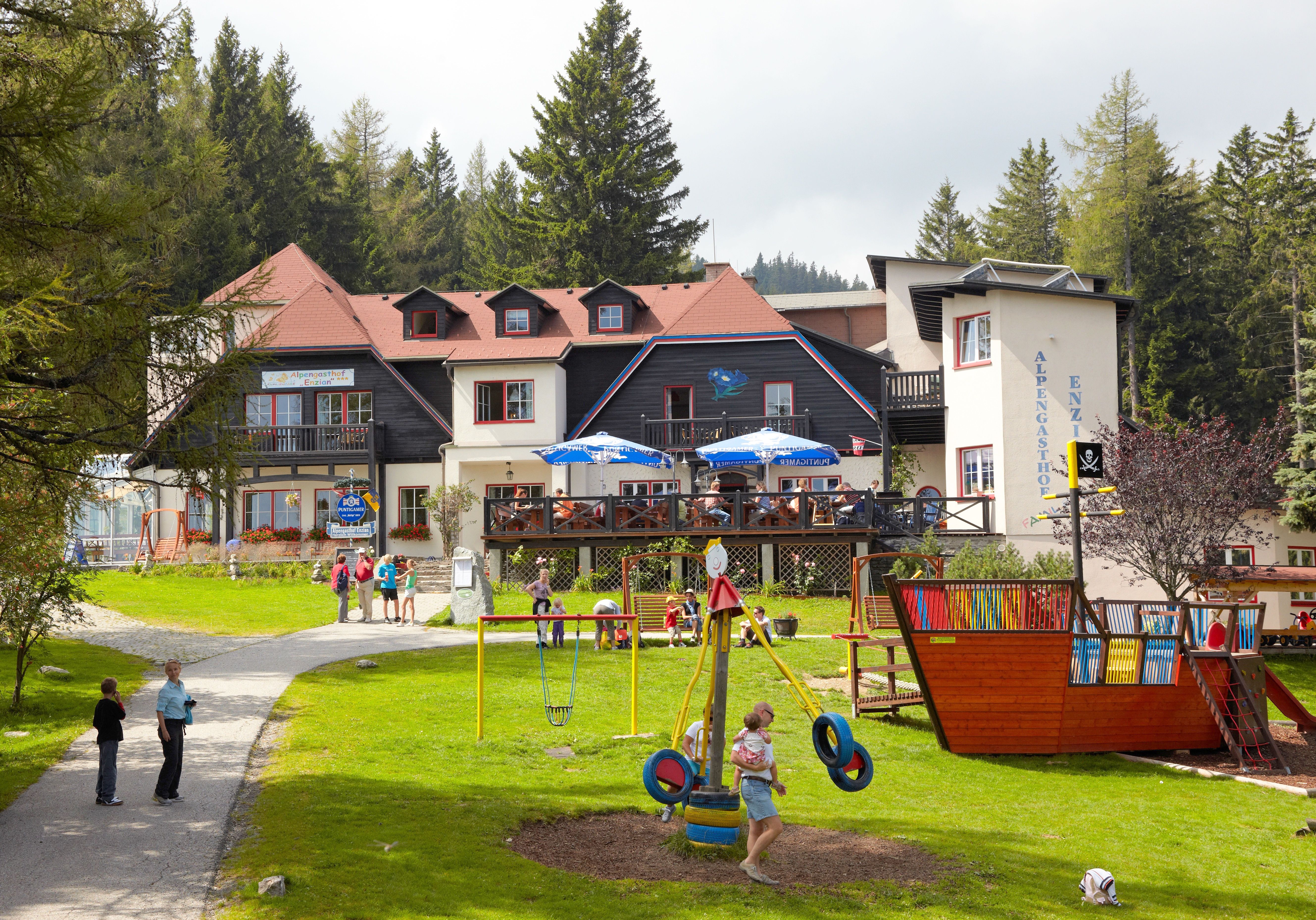 An inn in the Alps with a playground and outdoor people.
