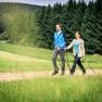 A couple Nordic walking on a country lane in front of a forest.
