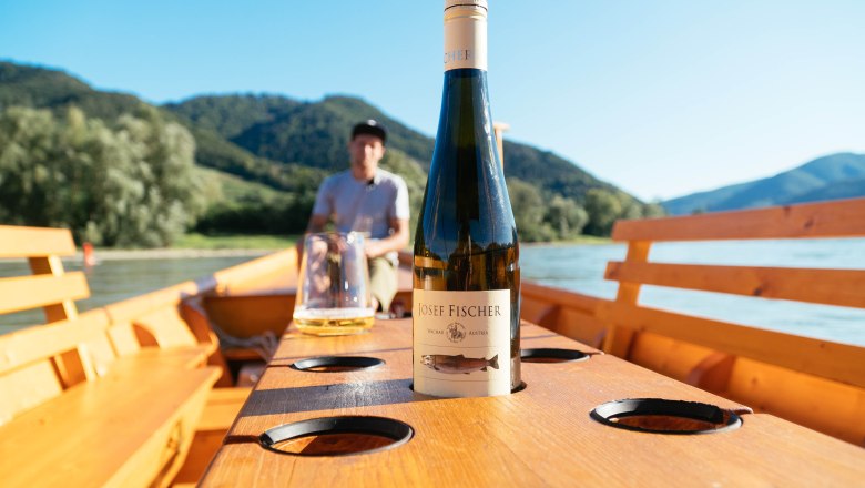 Wine bottle on a boat table with blurred background of mountains and a man.